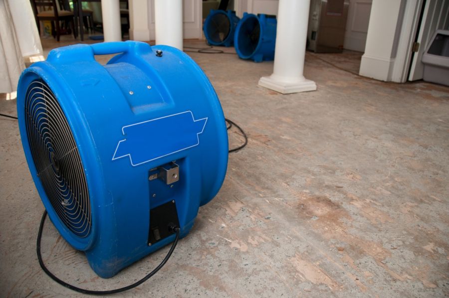 Blue industrial air mover drying a water-damaged room with stripped flooring during restoration work